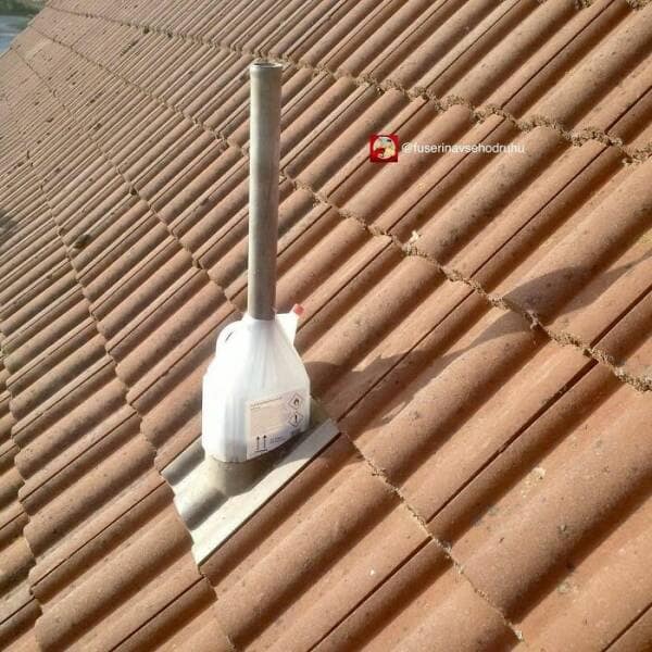 A silver vent pipe on a red tiled roof that has been improperly sealed and waterproofed with a cut-open plastic milk jug.