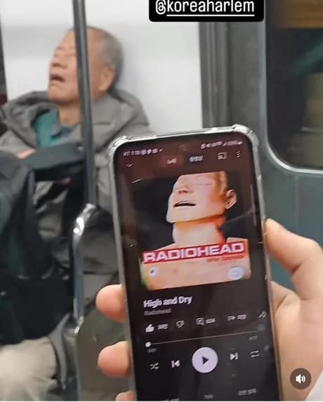 Sleeping subway rider mirrored by The Bends cover on a phone; look-alike gag.