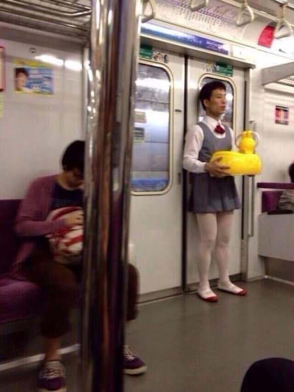 A famous photo of a man on a Japanese subway who is dressed in a traditional schoolgirl's uniform and is holding a large, inflatable, yellow rubber duck in his arms.