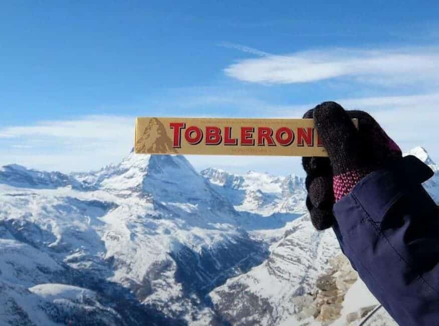 A Toblerone chocolate bar logo held up to perfectly match the real Matterhorn mountain in the snowy background.