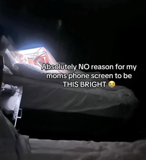 A very relatable and funny video still of a mom using her phone in a dark bedroom with the screen brightness turned all the way up.