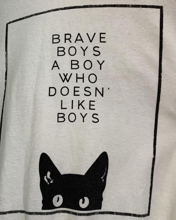 T-shirt with a black cat graphic and a jumbled slogan reading “BRAVE BOYS A BOY WHO DOESN’ LIKE BOYS.”