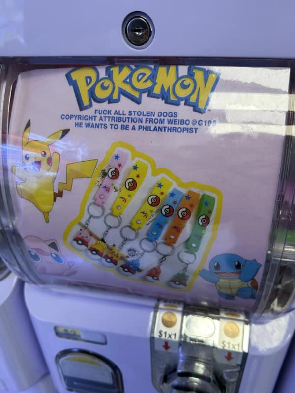 Gachapon machine poster using Pokémon art with a bizarre anti–dog-theft message above keychain options.