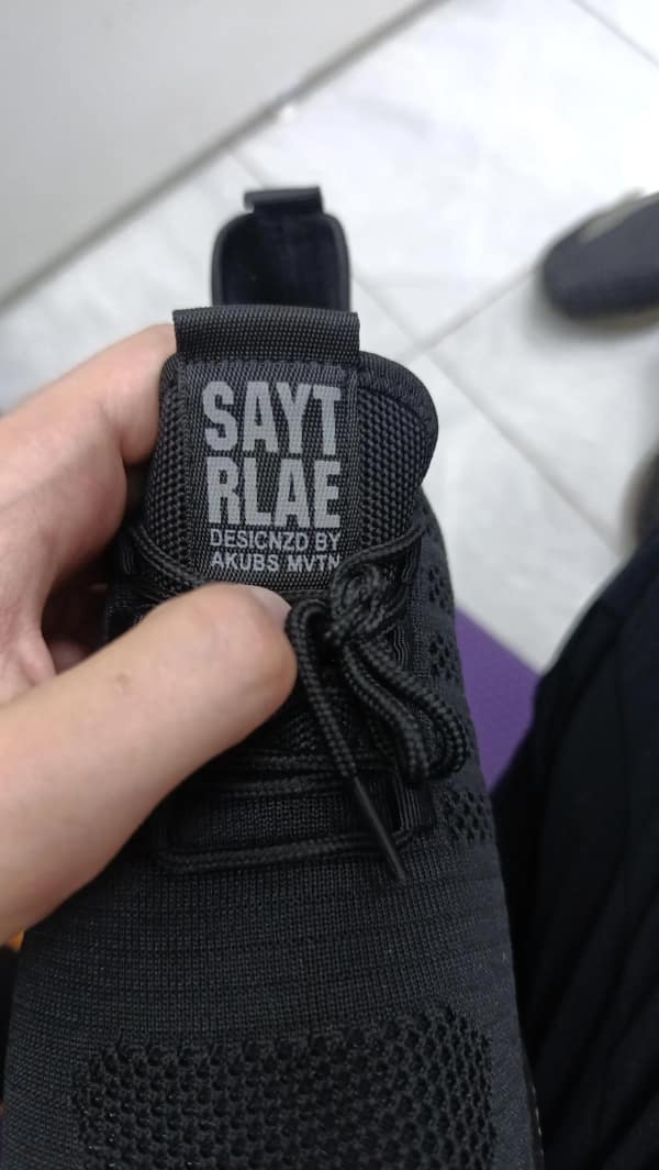 Sneaker tongue label with scrambled brand text: “SAYTR RLAE – DESIGNZD BY AKUBS MVTN.”