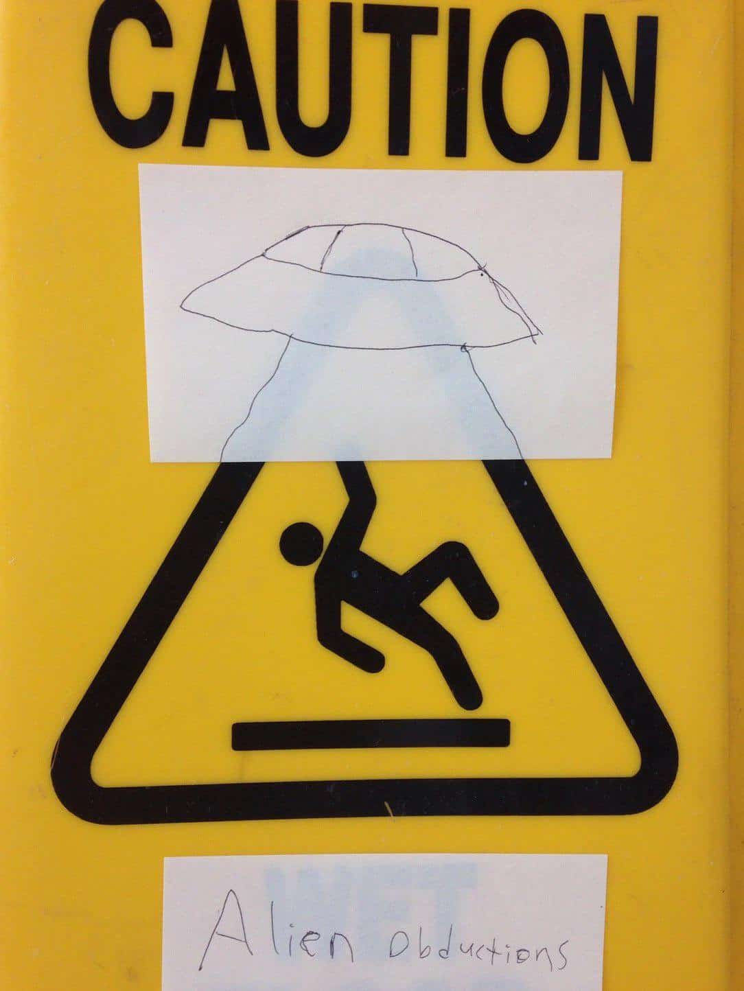 Wholesome graffiti on a wet floor sign, turning the falling person into a victim of an alien abduction.