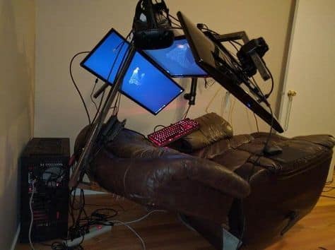 An incredibly elaborate and chaotic gaming rig with multiple monitors, controllers, and a VR headset all built around a comfortable leather recliner.