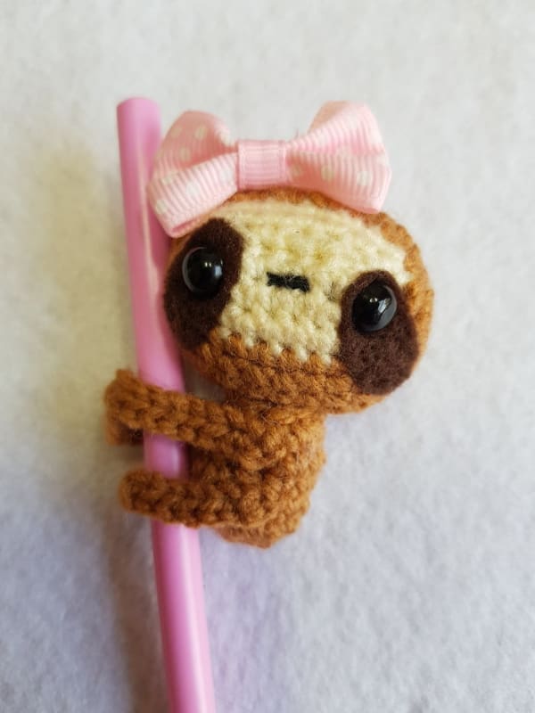 An adorable crocheted sloth with a pink bow designed to hug a pen, a cute DIY win.