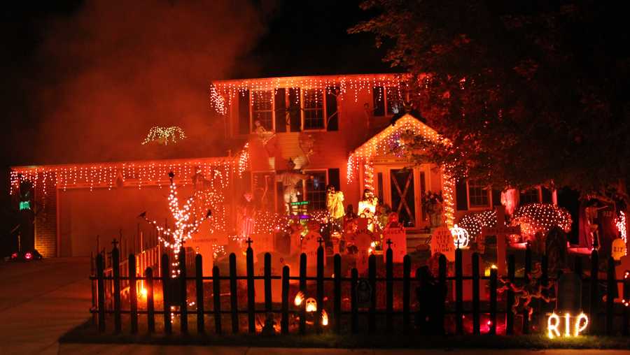 An amazing halloween house bathed in red light, with fog and a spooky graveyard fence in the yard.