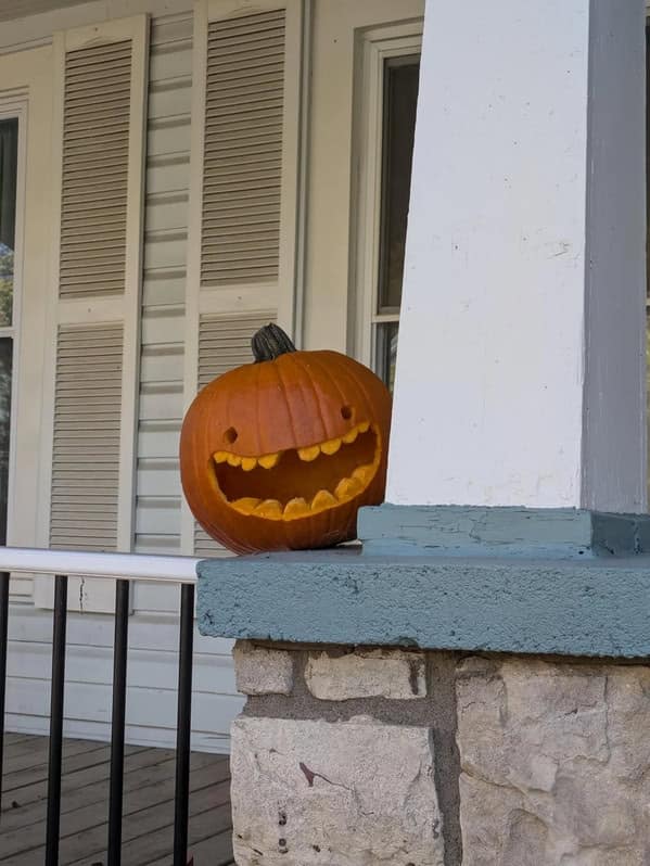 A simple but amazing pumpkin carving with a huge, toothy grin peeking around a porch column