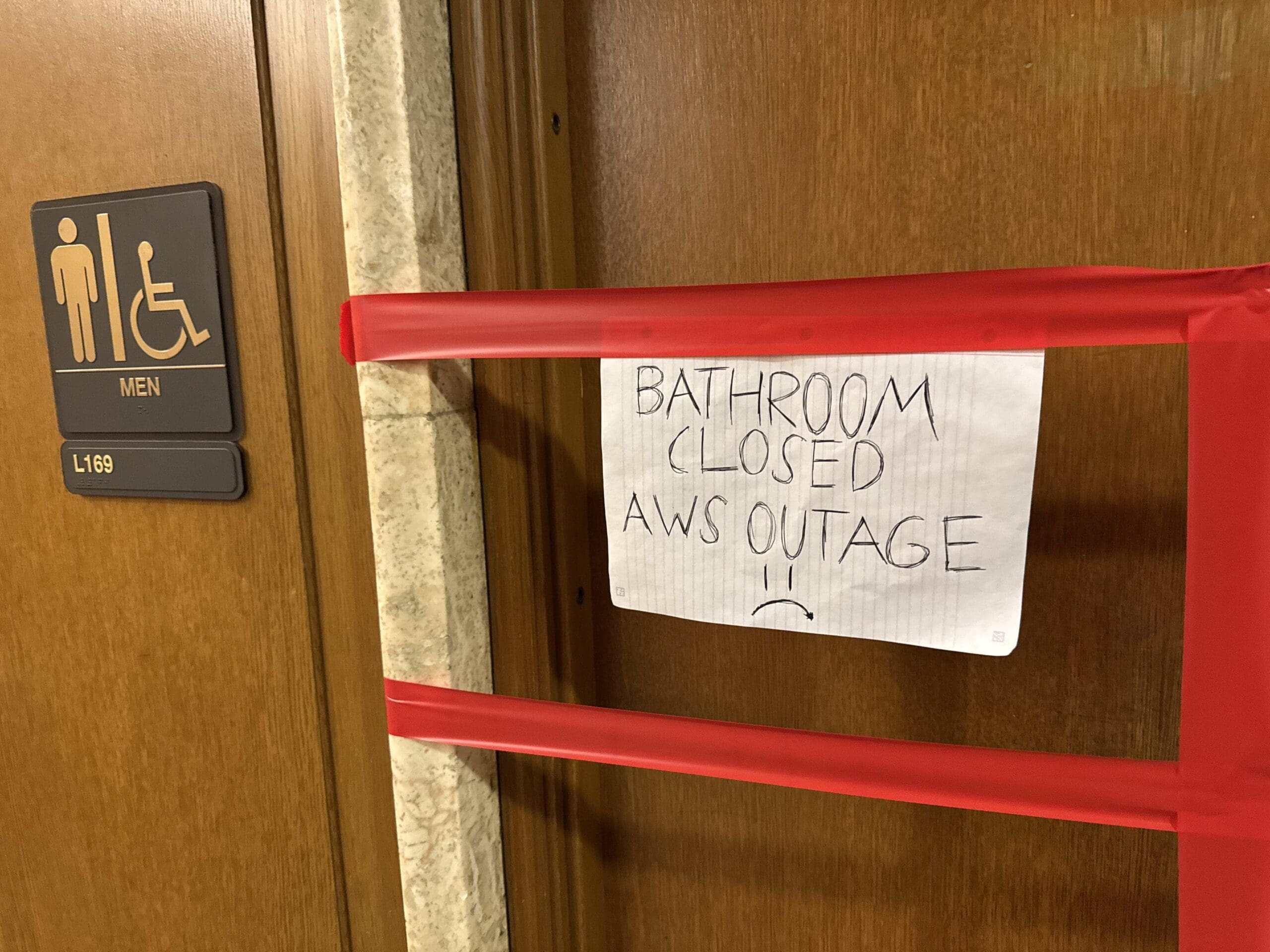 A funny AWS outage meme sign on a bathroom door blaming the closure on the recent outage.