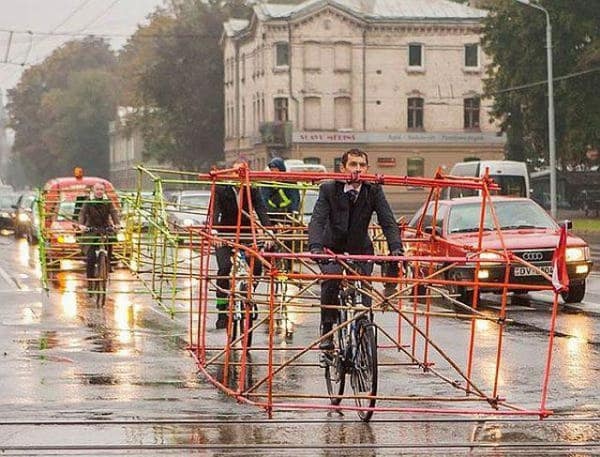 Cyclists riding bikes enclosed in large, colorful car-shaped frames made of bamboo for visibility and safety.
