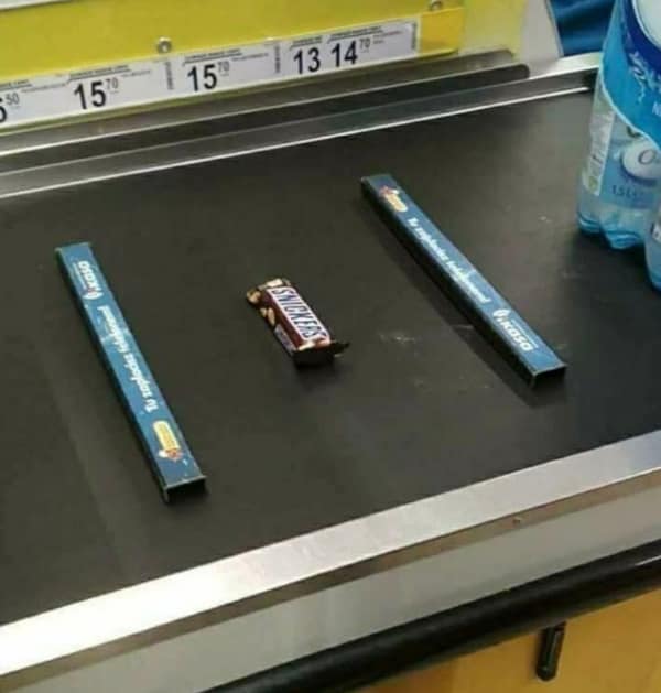 A single Snickers bar meticulously separated by two grocery checkout dividers on the conveyor belt.