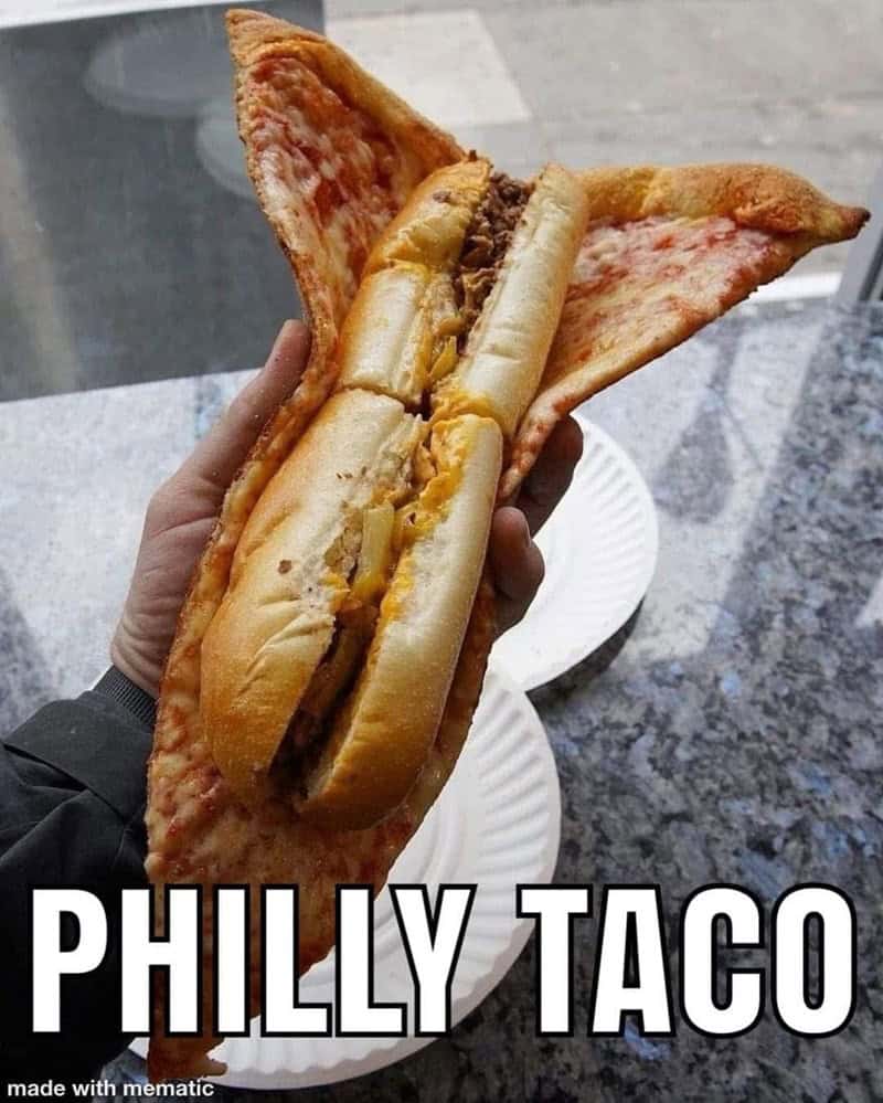 A hand holding a "Philly Taco," which is a Philly cheesesteak sandwich wrapped inside a folded pizza slice.