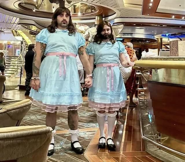 Two bearded men holding hands dressed in matching blue dresses as the Grady twins from The Shining.