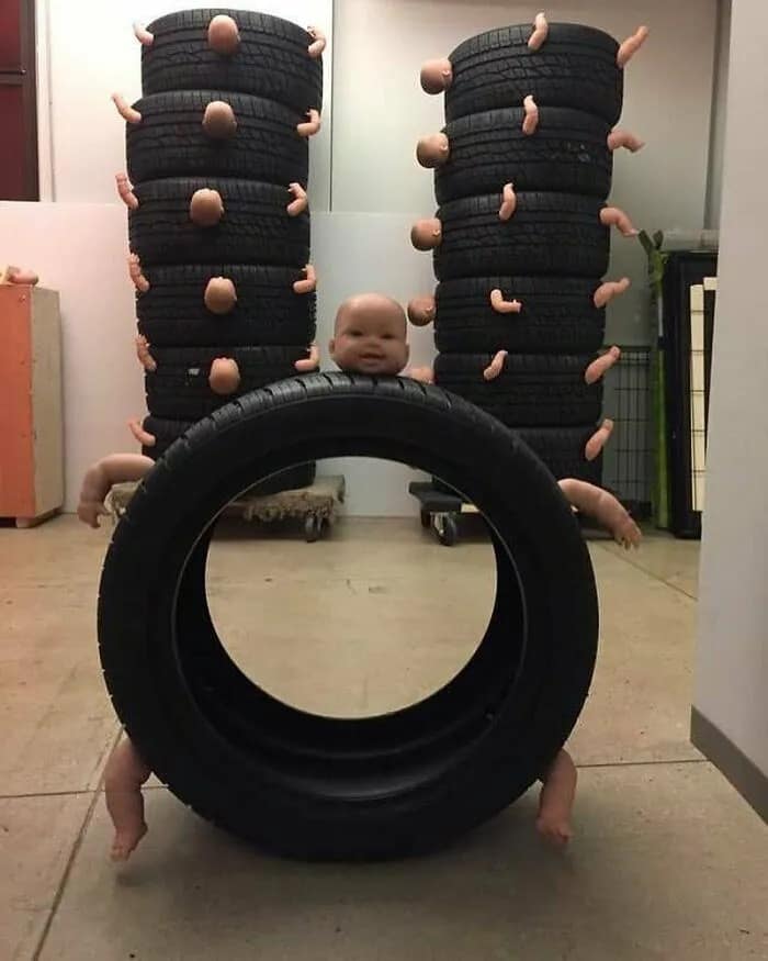 Truly cursed image showing unsettling sculptures made from stacked tires and dismembered baby doll parts