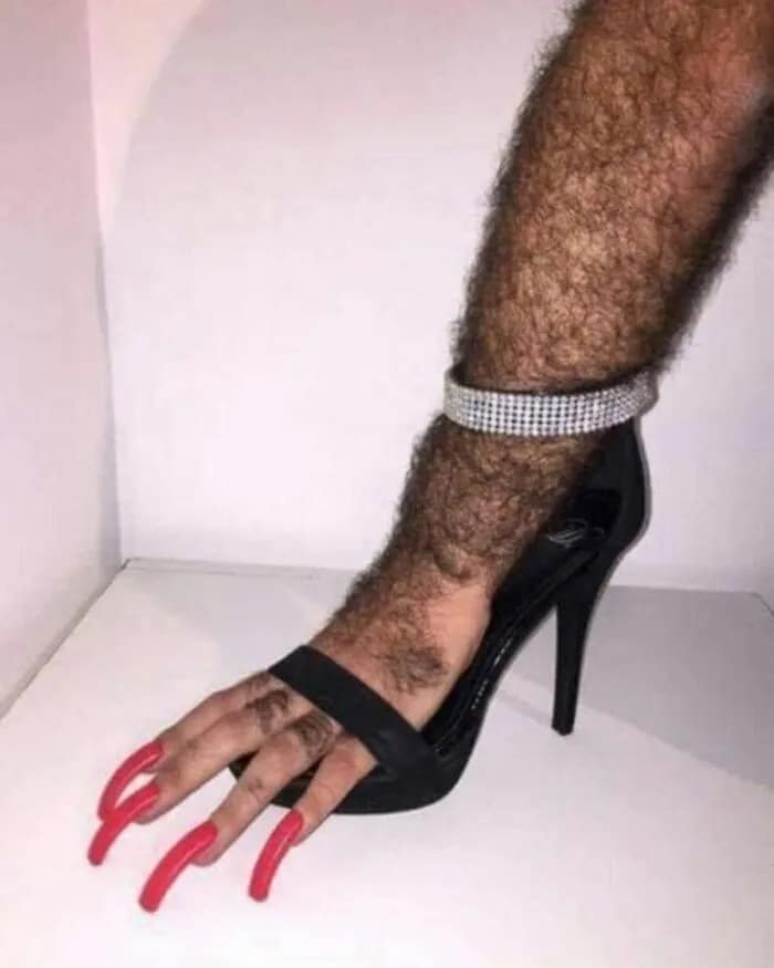 A cursed image depicting a hairy leg wearing a high heel shoe with long red fingernails as toes.