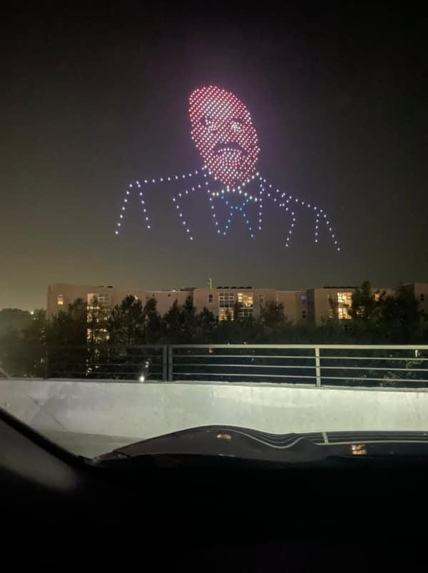 A cursed image of a giant, ominous face made of drones staring down from the night sky.