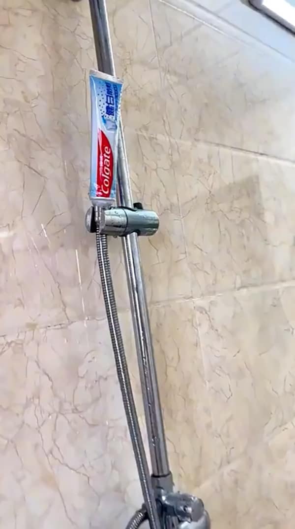 A DIY fail where a tube of Colgate toothpaste is being used to hold a shower caddy in place.