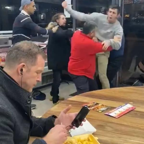 A funny food meme of a man calmly eating while a huge fight breaks out behind him in a restaurant.