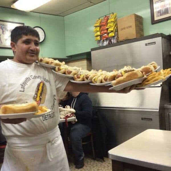 A food meme showing a waiter at Lafayette Coney Island impressively carrying about 20 hot dogs on his arms.