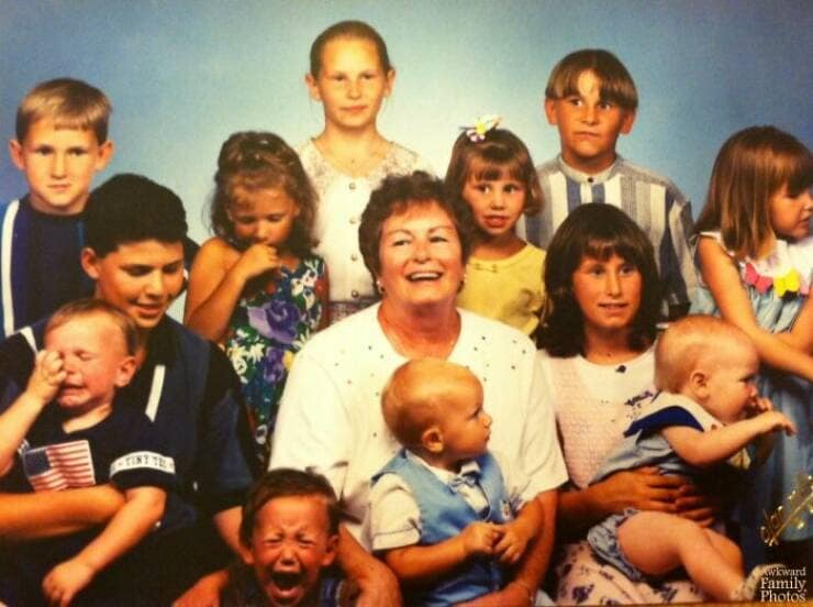 Awkward large family photo with a smiling grandma surrounded by many crying and unhappy grandchildren.