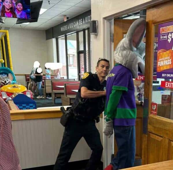 A funny and cursed image of the Chuck E. Cheese mascot being arrested by a police officer.