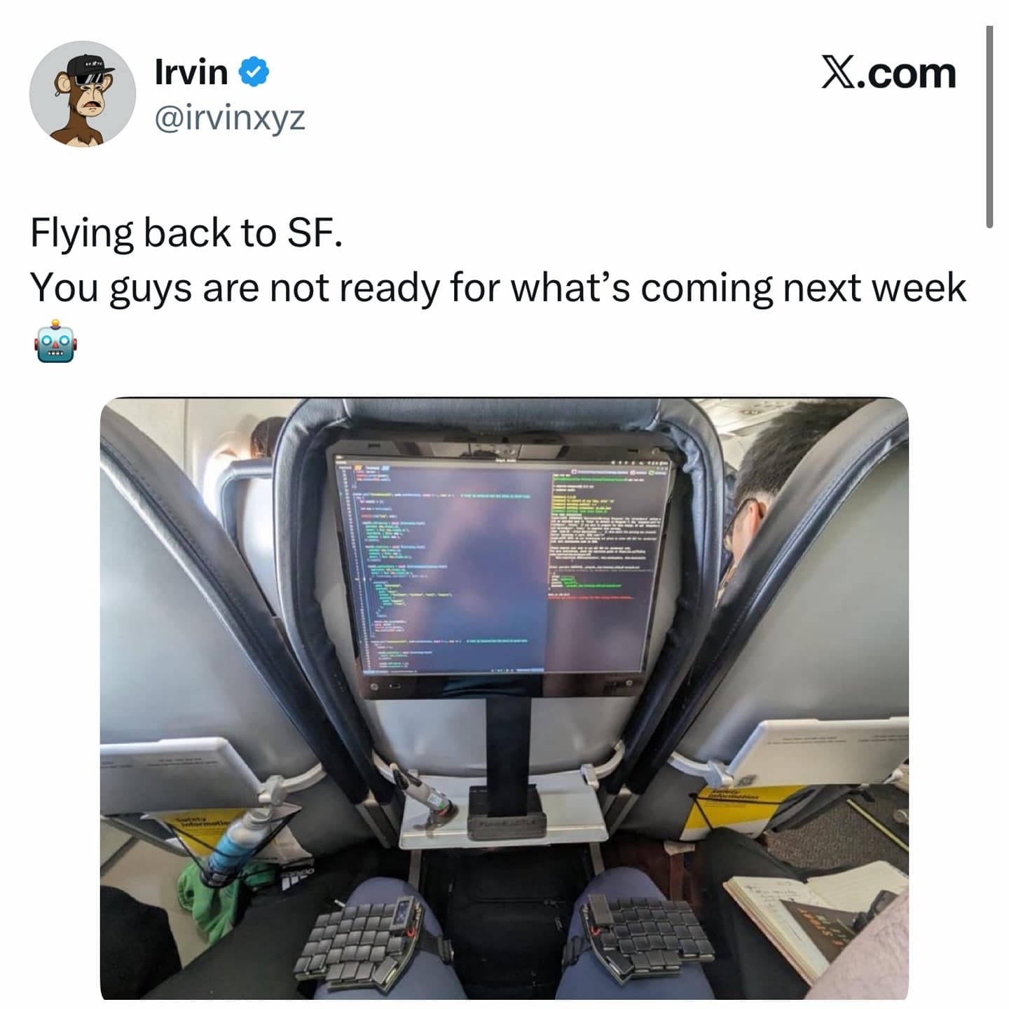 Funny pic of an extreme programmer setup on an airplane, including a large monitor and split keyboard.