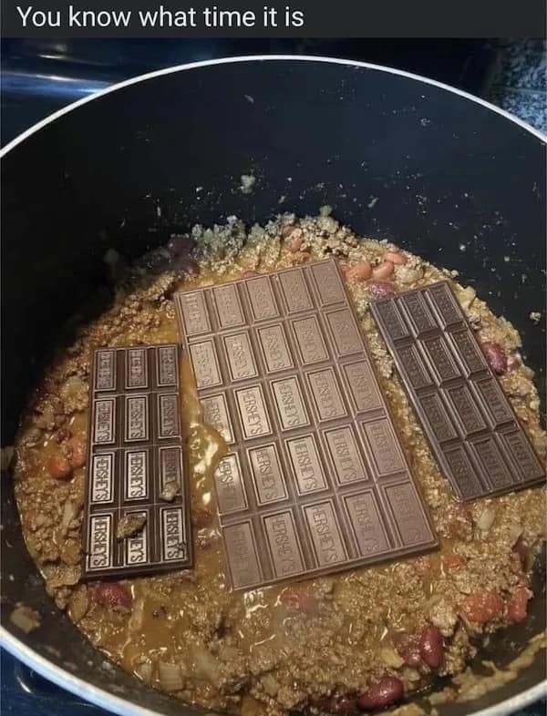 A cursed food photo showing someone putting whole Hershey's chocolate bars into a large pot of chili.