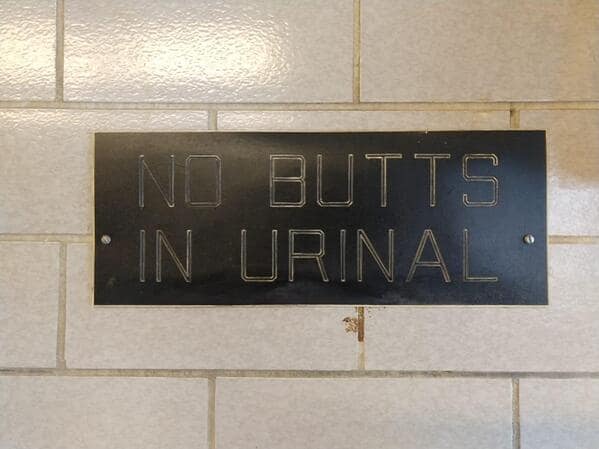 A bathroom sign that reads "NO BUTTS IN URINAL," an example of unintentionally funny signs.