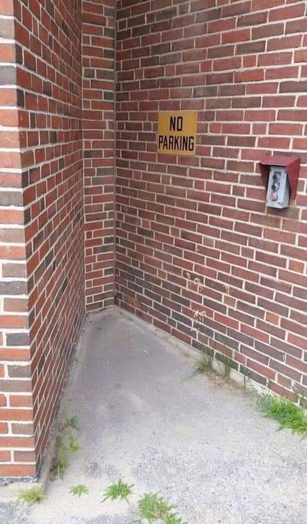 A completely useless "NO PARKING" sign posted in a tiny corner where no car could ever fit.