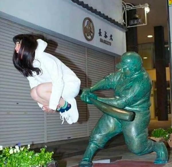 A hilarious no context image of a woman posing as if hit by a baseball player statue.