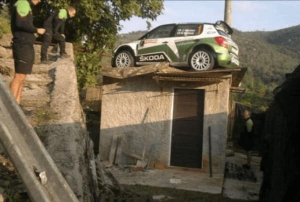 A weird no context image showing a rally car crashed on the roof of a small building.