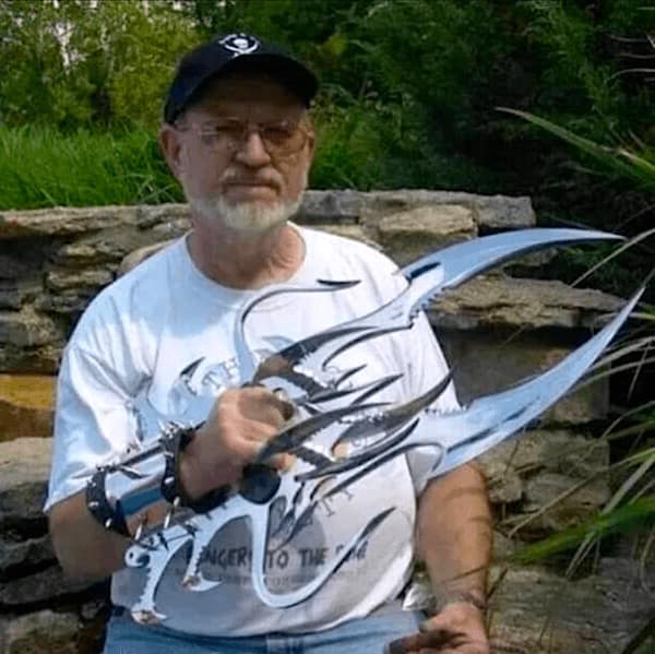 A cursed image of an older man seriously posing with giant, bladed claw weapons.