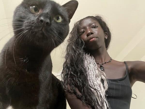 A young woman with braided hair takes a selfie with her sleek black cat, sharing a similar expression