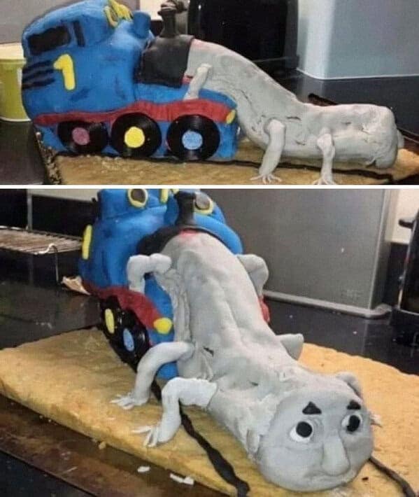 A nightmarish Thomas the Tank Engine cake that is fused with a long, gray, creature with a human face.
