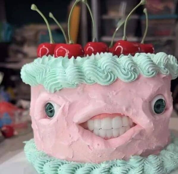 A terrifying pink birthday cake decorated with realistic fake eyeballs, a full set of dentures, and cherries.