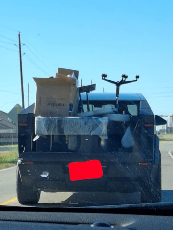 A futuristic-looking truck on the highway with a mess of unsecured junk in its bed.
