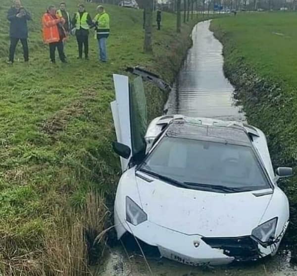 An expensive white Lamborghini supercar crashed nose-first into a muddy ditch, with the scissor door open.