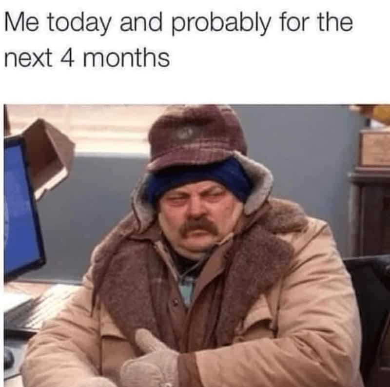 Ron Swanson from Parks and Rec bundled in multiple layers of winter clothes looking grumpy at his desk.