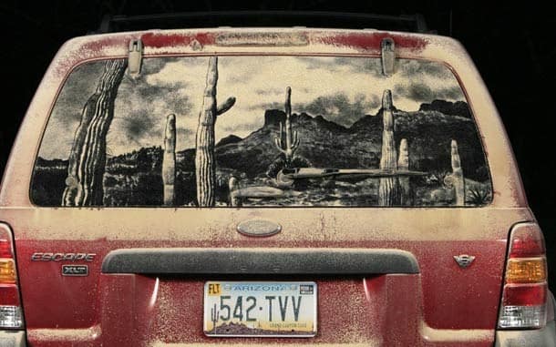 Detailed desert landscape with cacti drawn in dust on a red Ford Escape rear window.