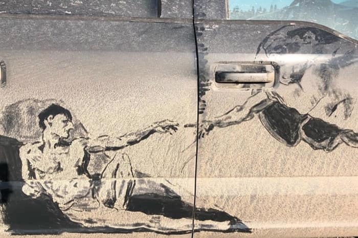: Michelangelo's Creation of Adam recreated in dirt on the side doors of a truck.