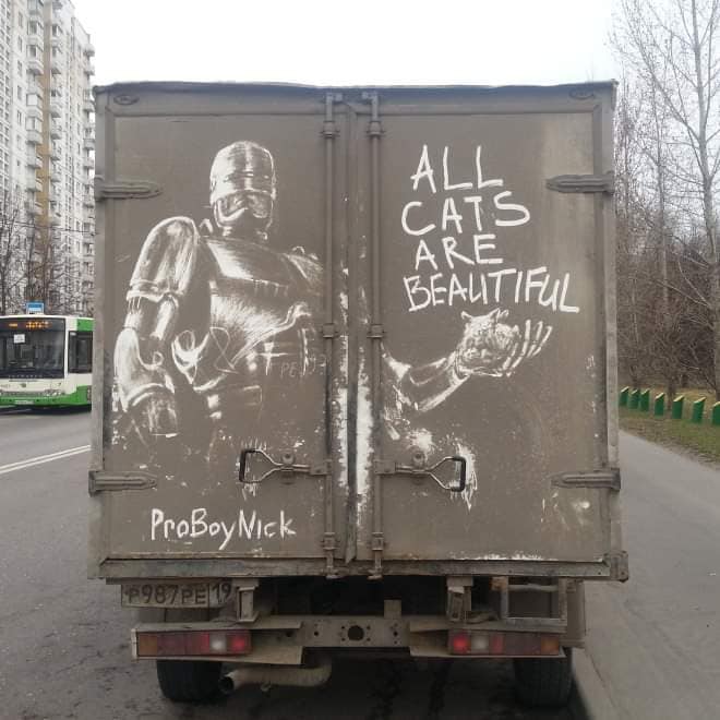 Robocop sketched in dirt on a truck back door with text All Cats Are Beautiful.