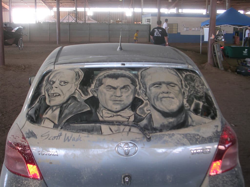 Phantom of the Opera, Dracula, and Frankenstein drawn in dust on a Toyota hatchback.