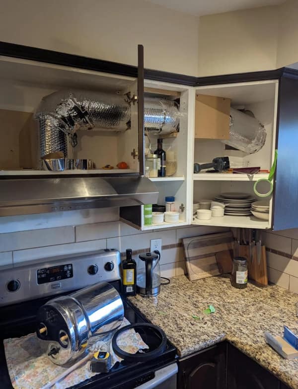 A diy fail showing silver ductwork crammed dangerously into a kitchen cabinet.