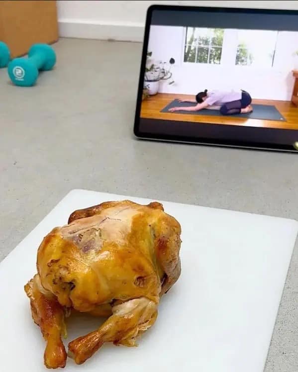 Roasted chicken on cutting board appearing to do yoga pose while watching tablet video.