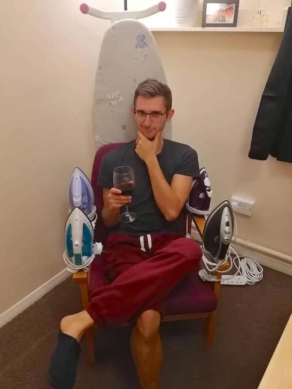 A man holding a wine glass, sitting on a chair decorated with household irons to look like the "Iron Throne."