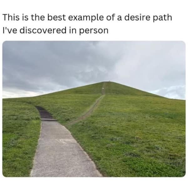 A photo showing a perfect example of a "desire path" where people ignore the winding sidewalk to walk straight up a grassy hill.
