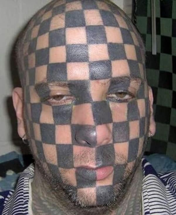 Man with a black and grey checkerboard pattern tattooed over his entire face.