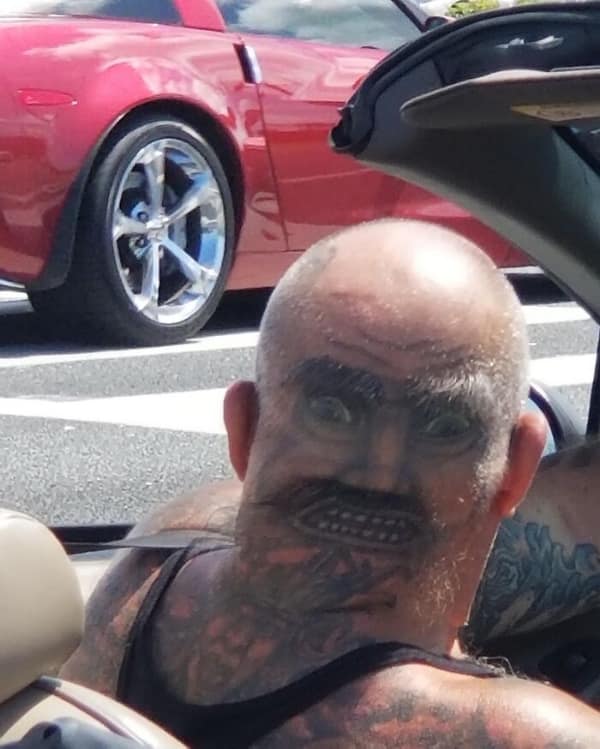 Face tattoo of a man with a mustache inked on the back of a bald head.