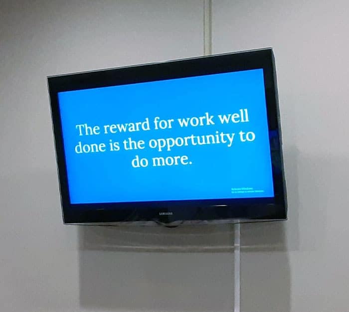 TV screen displaying quote stating the reward for hard work is just more work.